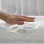 A contoured memory foam pillow designed for ergonomic neck and head support sits on a neatly made bed in a calming bedroom environment. The pillow features a curved shape that promotes proper spinal alignment, pressure relief, and sleeping comfort. Soft, breathable fabric and supportive memory foam construction highlight its benefits for reducing neck pain, improving sleep quality, and providing stable support for individuals experiencing vertigo, dizziness, or nighttime discomfort.